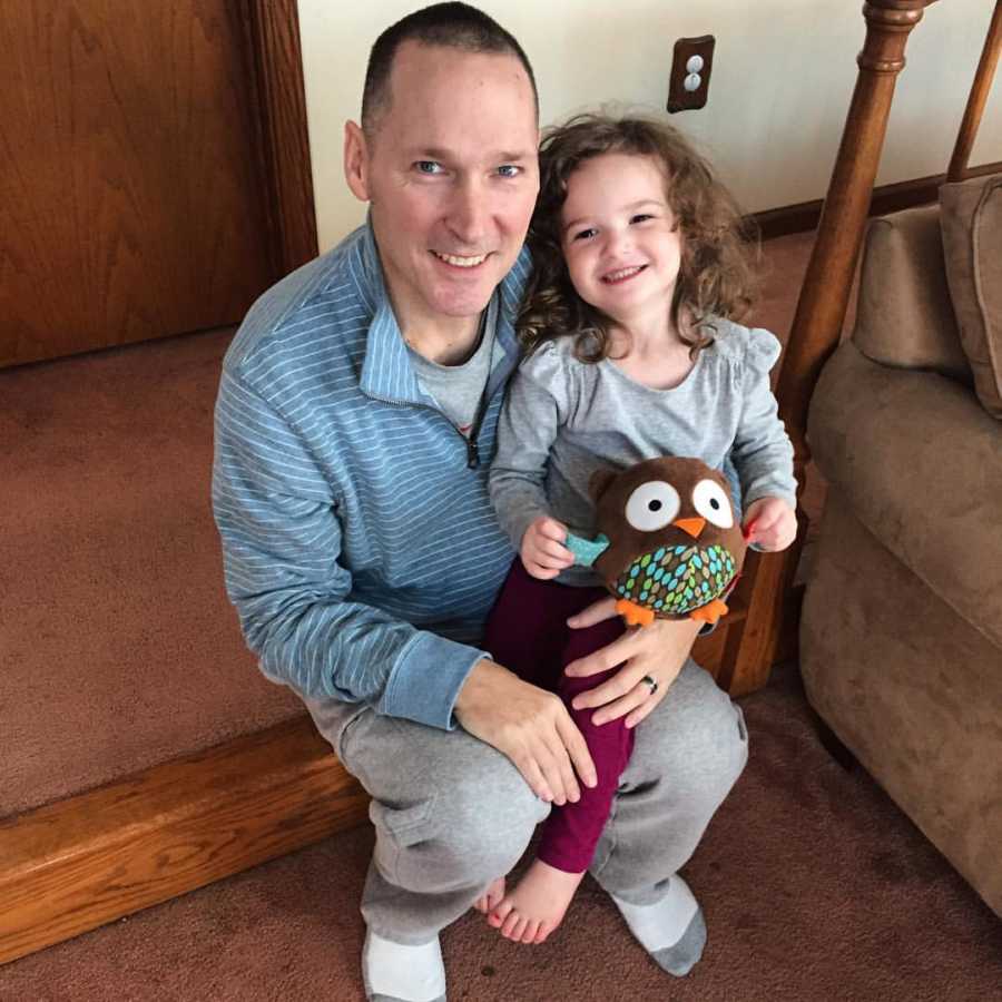 Man who has since passed sits on floor in home smiling with granddaughter sitting on his lap