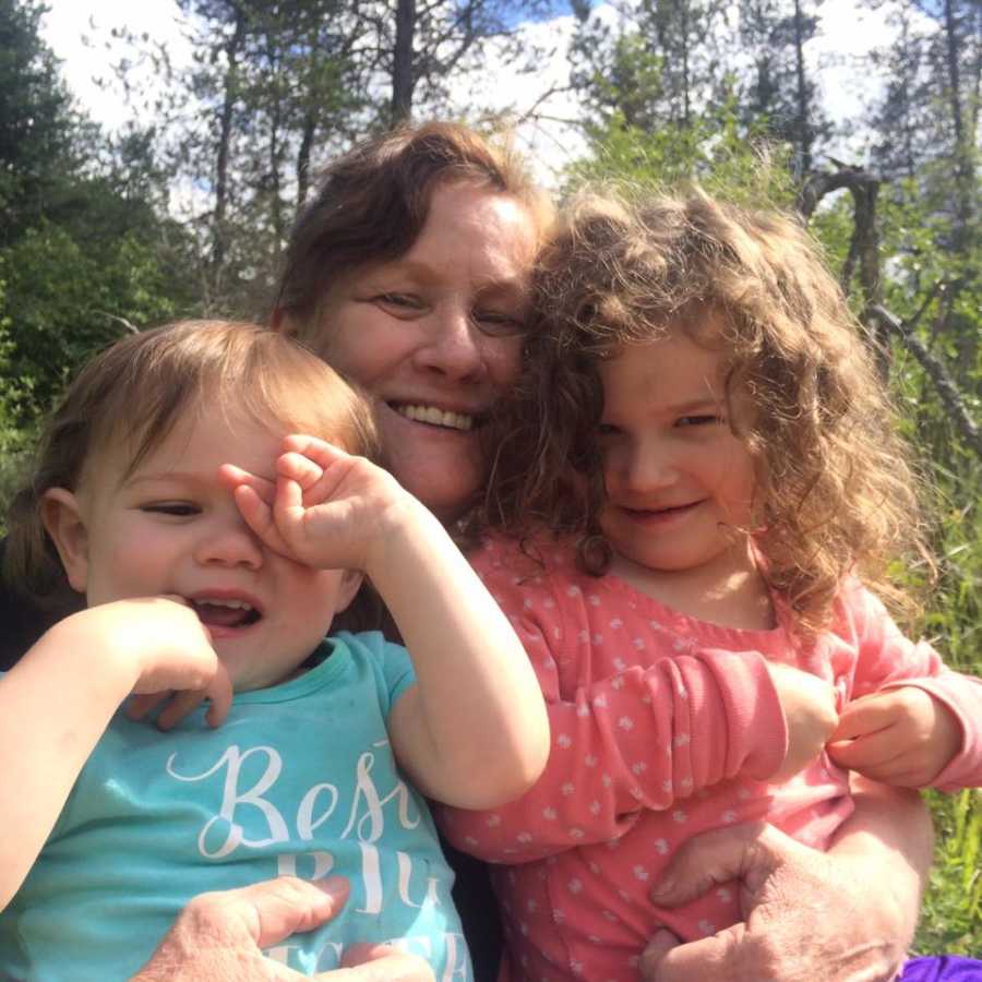 Grandmother sits smiling with two granddaughter's in her lap