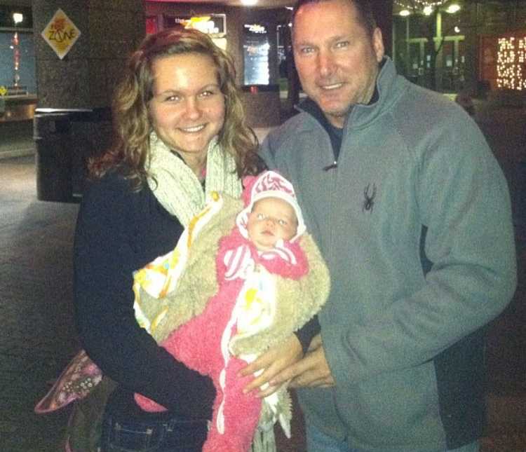 Woman stands holding her baby daughter with father beside her