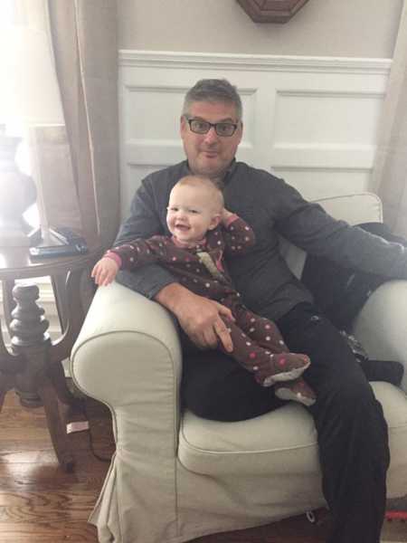 Grandfather sits in chair with toddler granddaughter in his lap