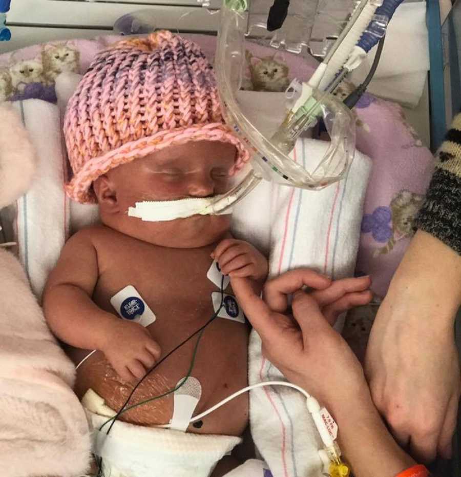 Newborn who has since passed wears pink knit hat in NICU holding on to her mother's finger