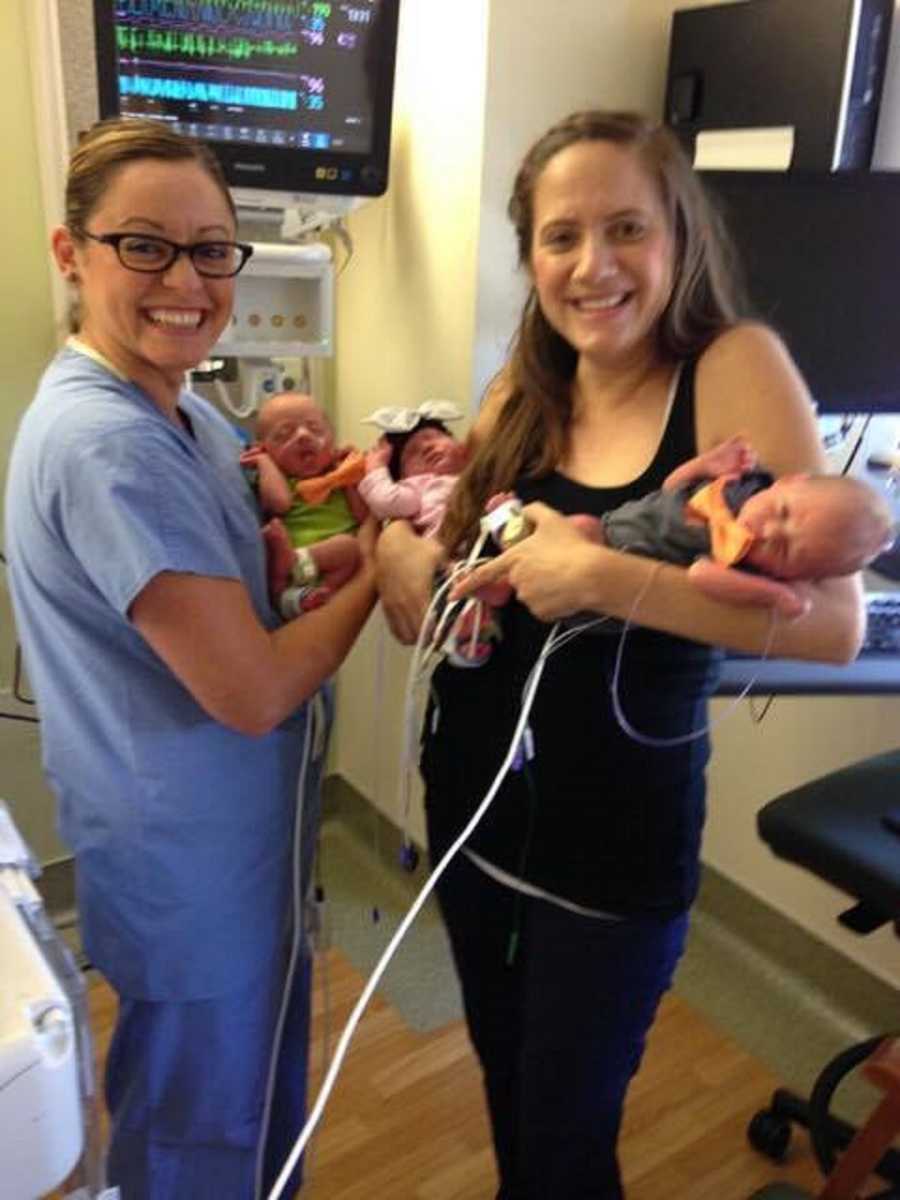 Mother who just gave birth holds two of her triplets while the nurse holds the other