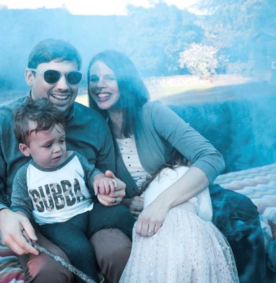 Man with bone marrow disease sits smiling with son on his lap beside wife and daughter