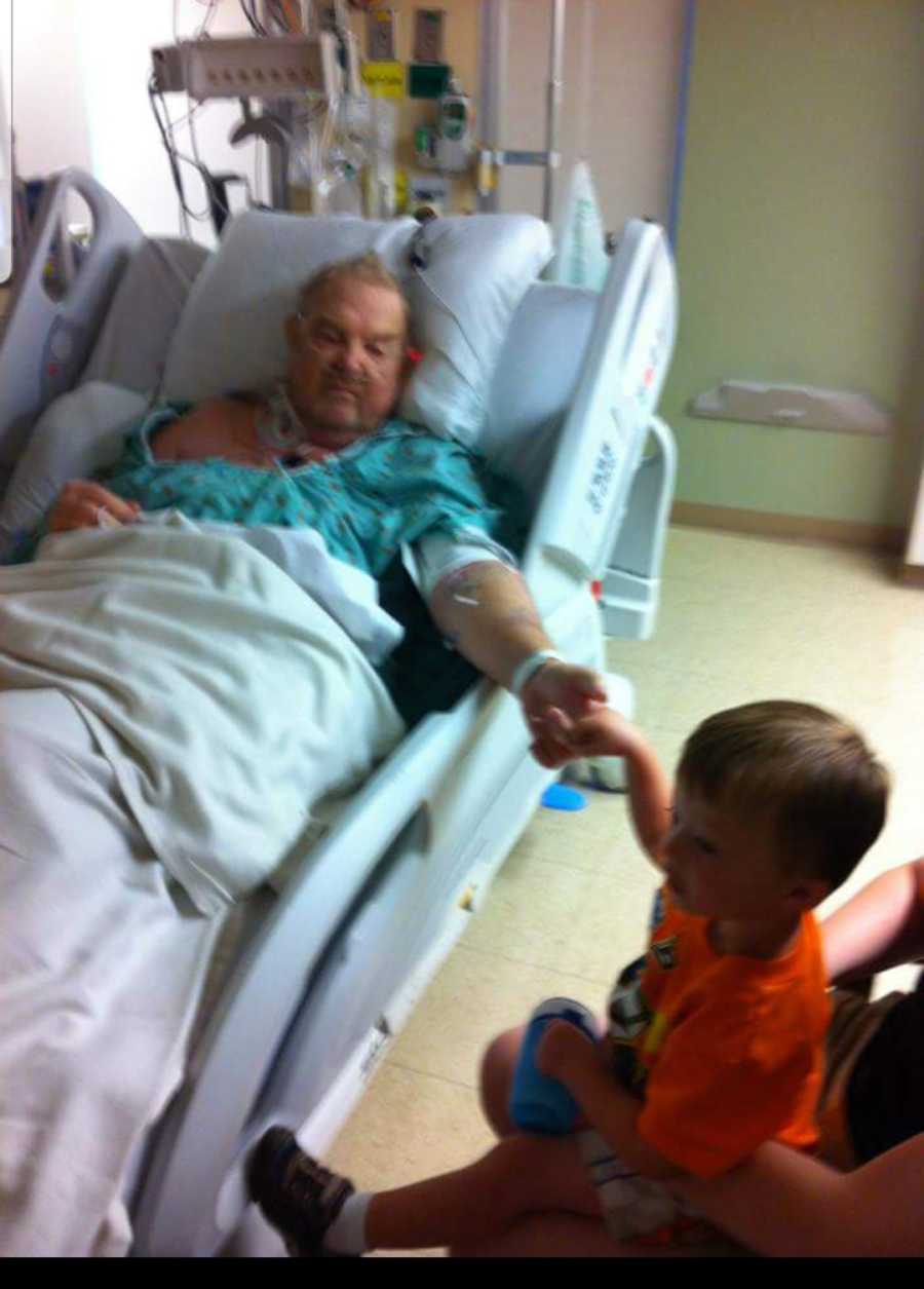 Grandfather who just had stroke lays in hospital bed holding grandson's hand