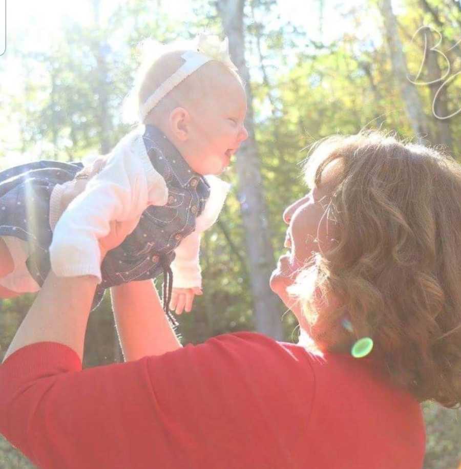 Mother smiles as she holds up baby daughter in the air