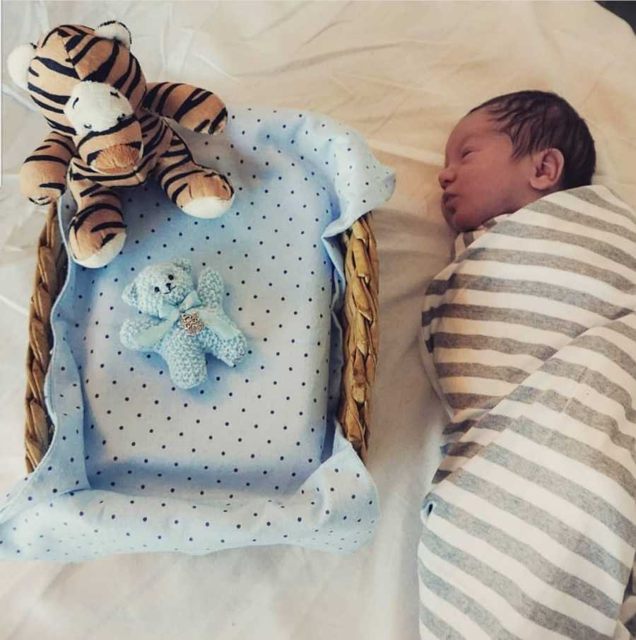 Newborn sleeps swaddled in blanket beside basket where his twin who was absorbed in womb would be