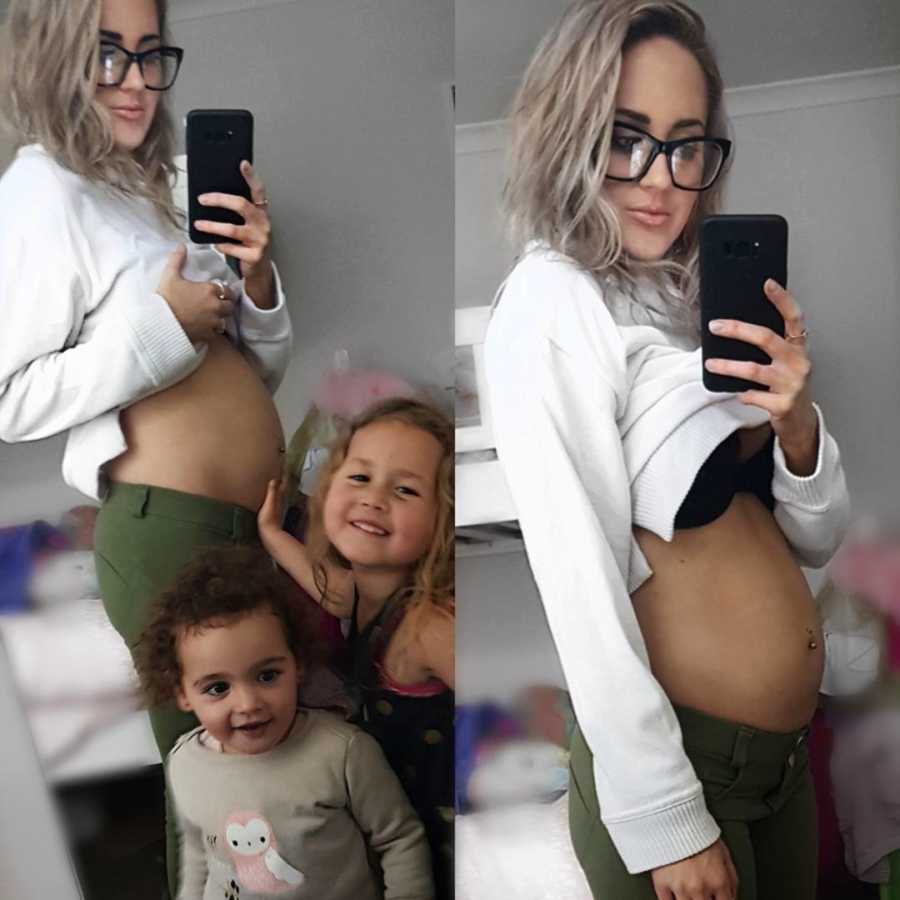 Pregnant woman takes mirror selfie with her two young daughter standing in front of her