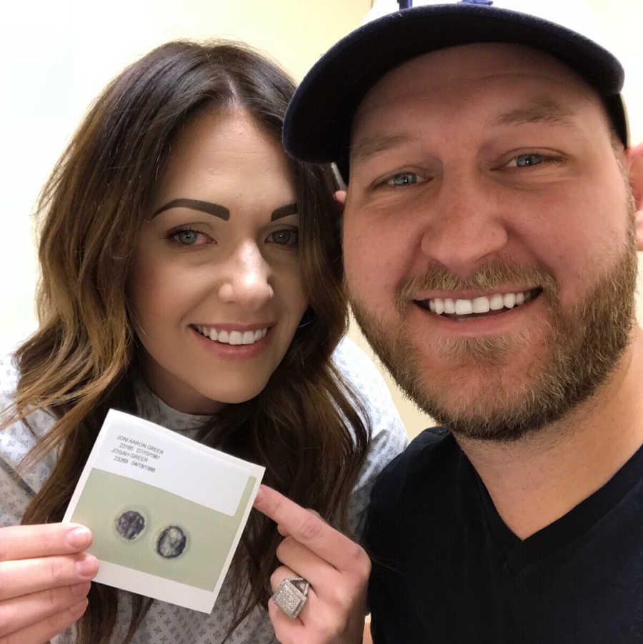 Husband and wife smile in selfie holding up sonogram of successful embryo implantation