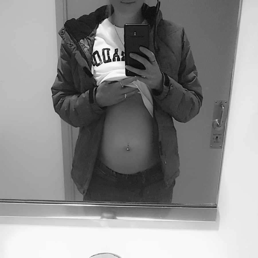 Pregnant woman takes mirror selfie holding up shirt to show stomach