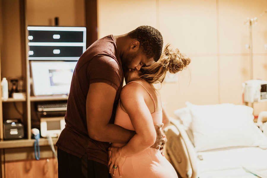 Husband hugs pregnant wife as they stand in hospital room