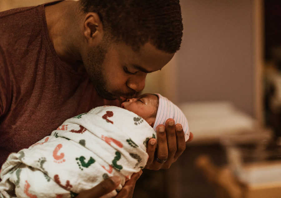 Father holds newborn in his arms and kisses her on the head