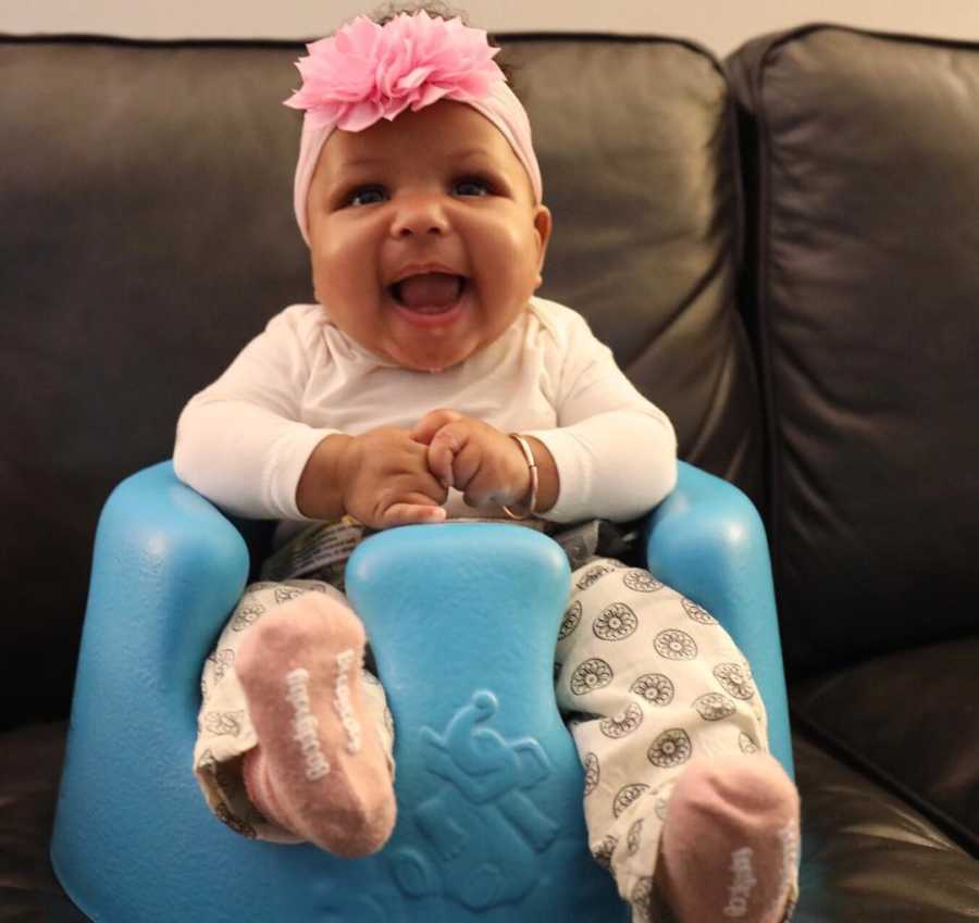 Infant whose adopted mother faced many miscarriages sitting in baby chair on couch smiling 