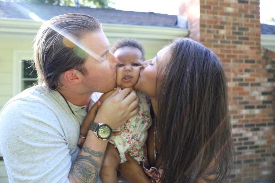 Husband and wife who had several miscarriages hold up adopted baby kissing her cheeks