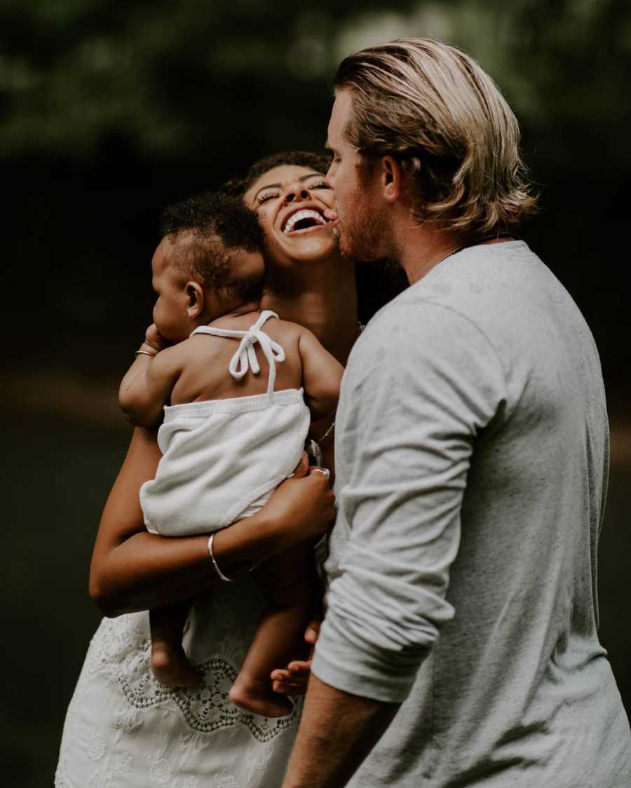 Mother who had multiple miscarriages holds adopted daughter smiling beside husband