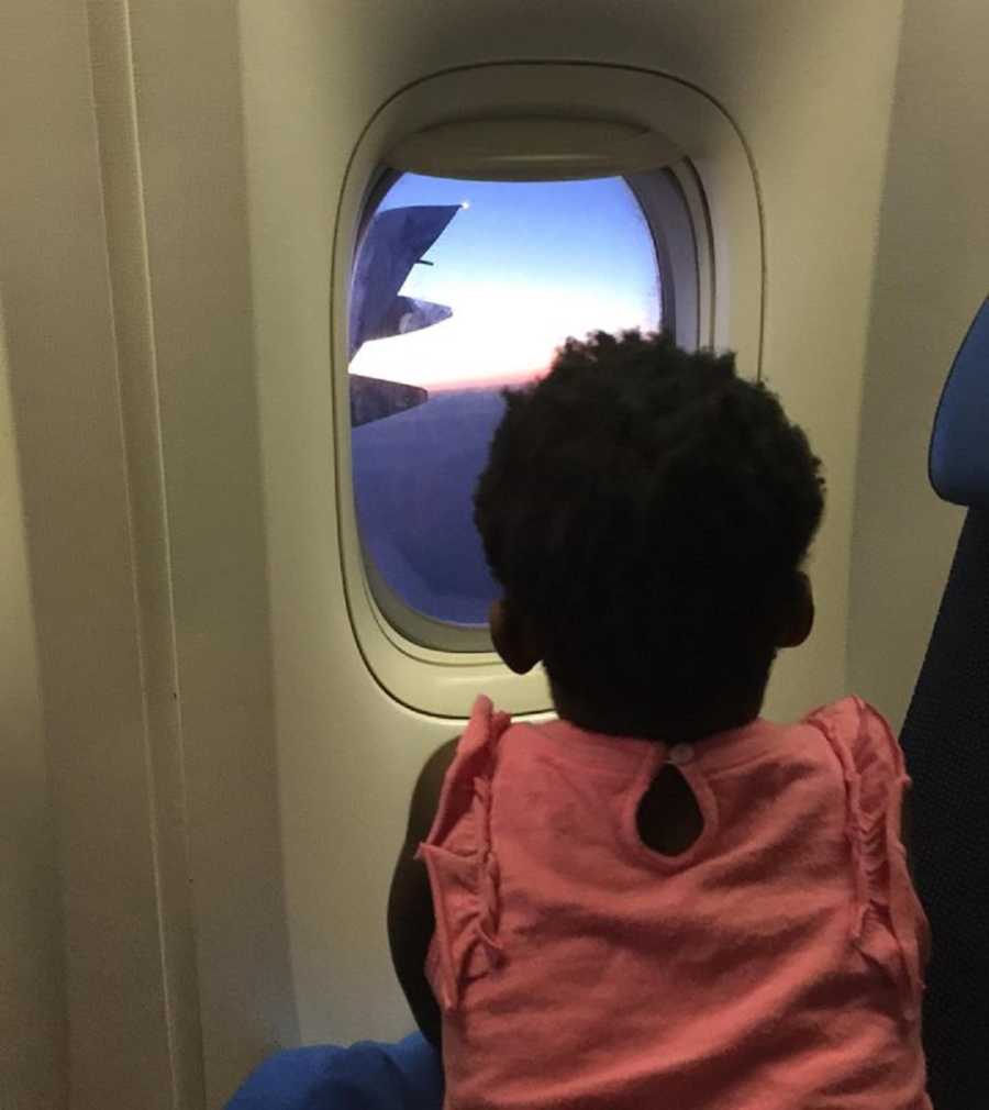 Adopted toddler from Ghana sits on plane looking out window 