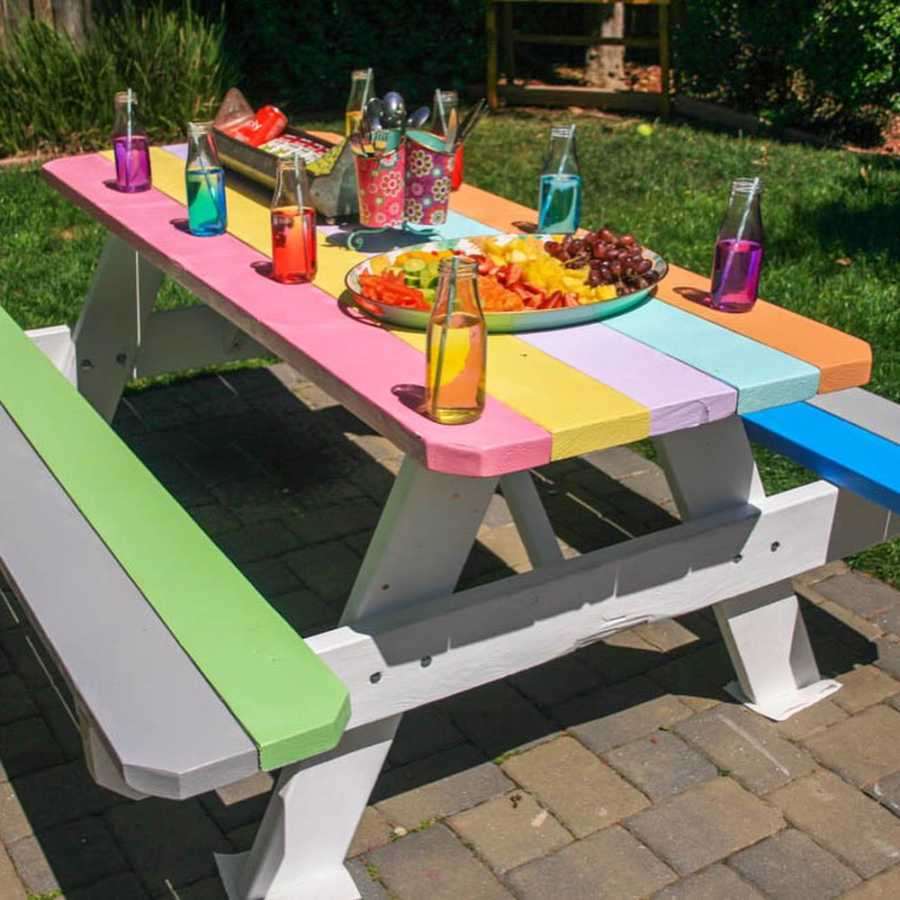 Rainbow painted picnic table with colorful drinks and food on it
