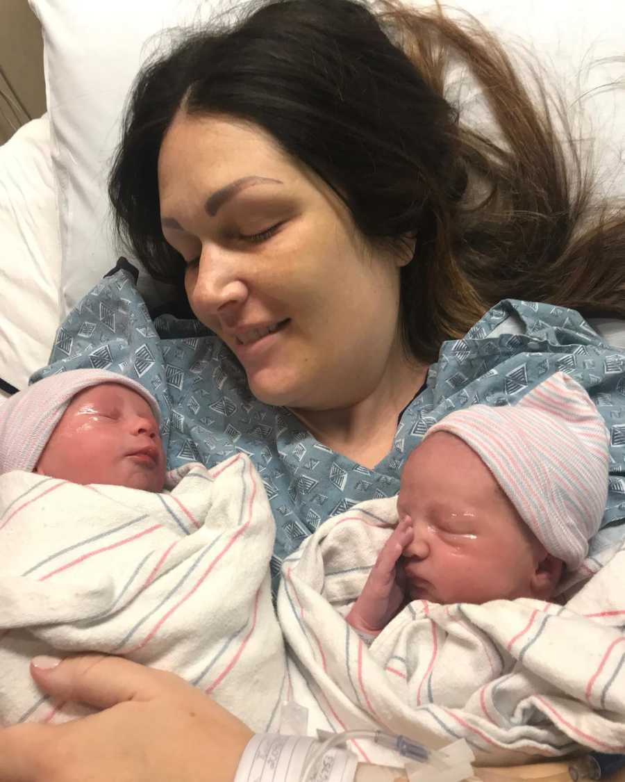 Woman who just gave birth smiles down at twins lying on her chest who were conceived through IVF