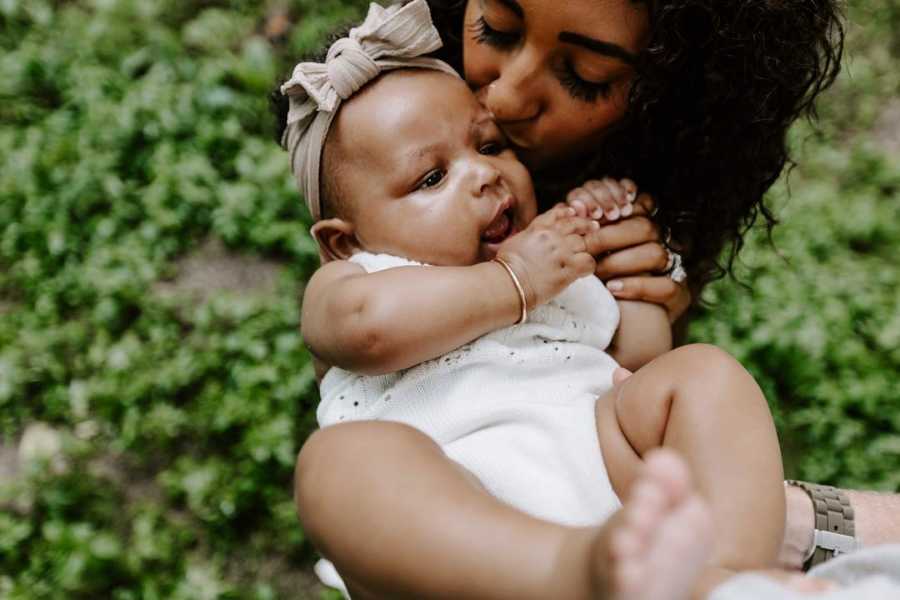 Close up of adopted infant being held and kissed on forehead by mother