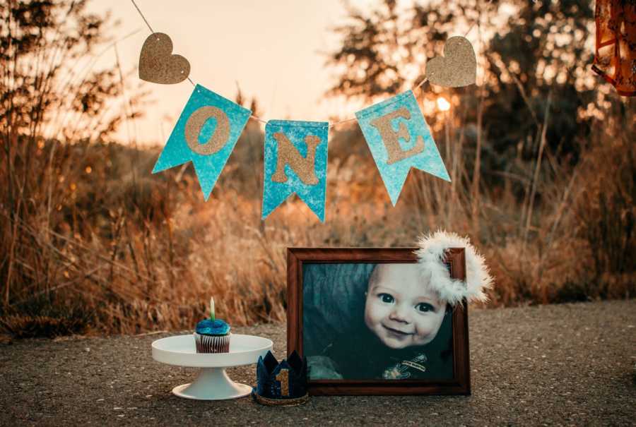 Picture frame of deceased 8 month old boy beside cupcake and banner that says, "One"