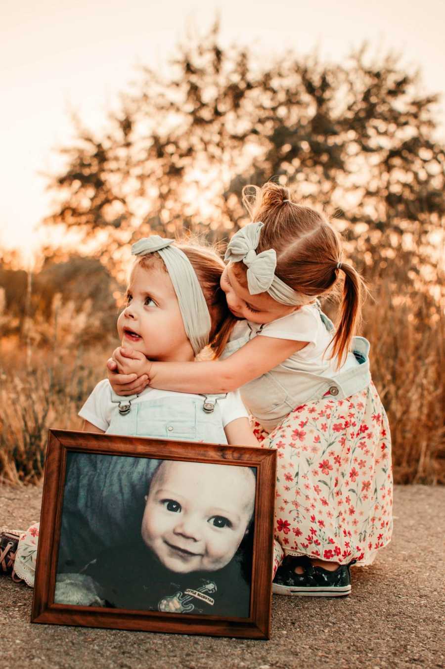 Picture frame of deceased 8 year old with his older sisters hugging behind it
