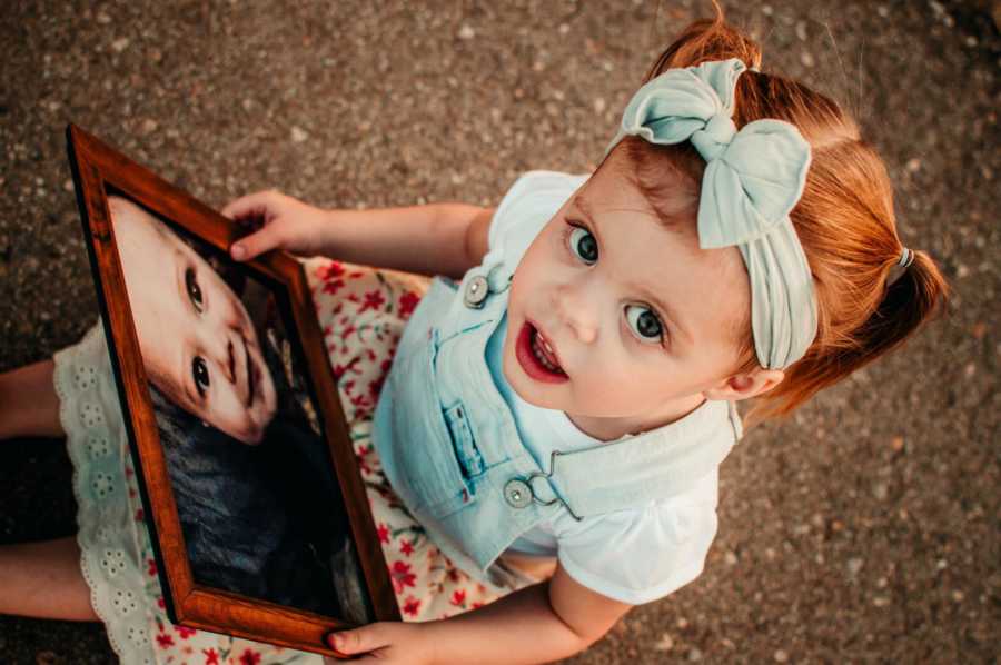 Toddler holding picture frame of her 8 month old brother who passed away