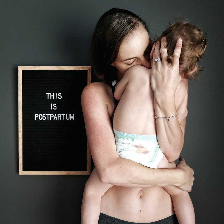 Shirtless woman holds baby to chest beside sign saying, "This is postpartum"