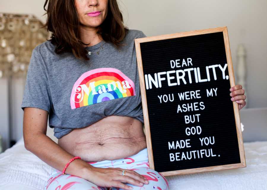 Woman who struggled with infertility holds sign saying, "Dear infertility you were my ashes but god you made me beautiful"