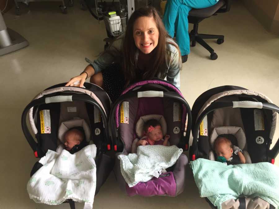 Woman who struggled to get pregnant sits on ground behind her newborn triplets in car seats