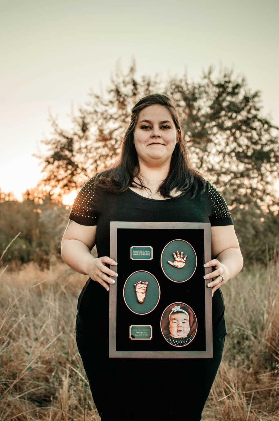 Pregnant mother holds bored up that contains deceased first born's hand and foot print and a picture of her