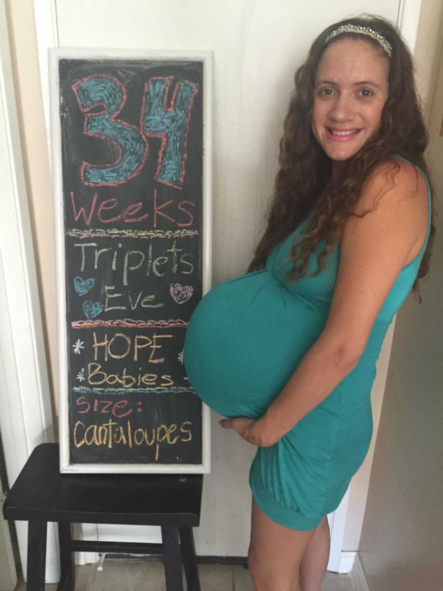 Pregnant woman who struggled with fertility stands next to sign that says, "34 weeks"