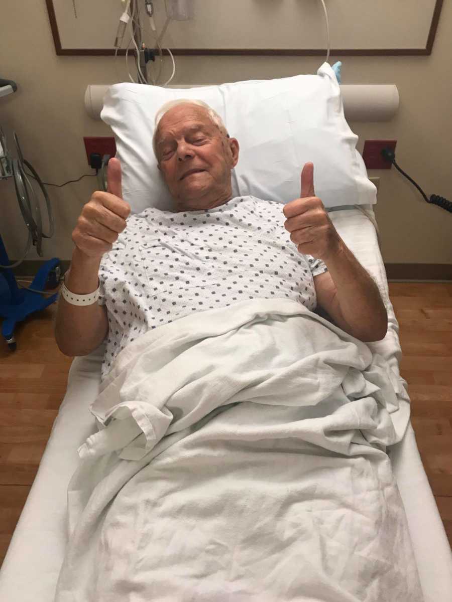 Elderly man lays in hospital bed with thumbs up before hernia surgery