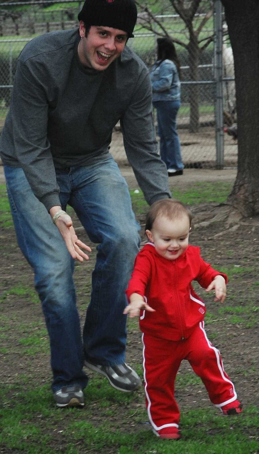 Single father smiling while walking behind toddler daughter in park