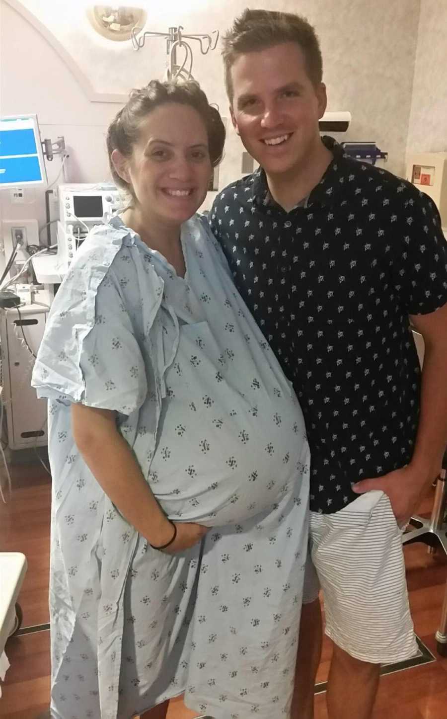 Pregnant woman who was told she was unfit to carry triplets stands smiling beside husband