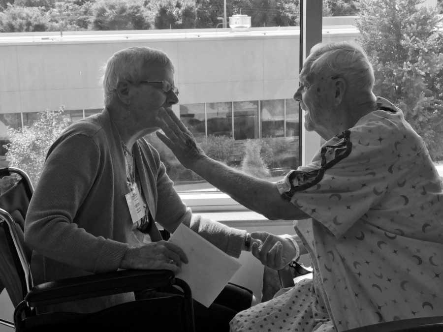 Elderly man who just had surgery sits in hospital gown reaching for wife who has dementia