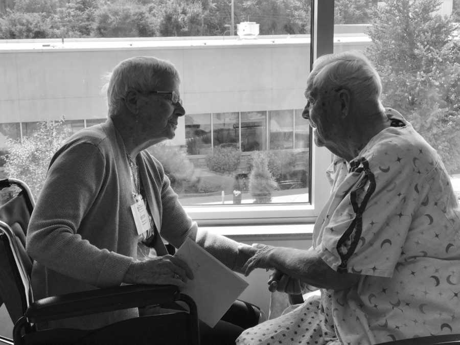 Woman with dementia sits in wheelchair holding hands with husband who just had surgery