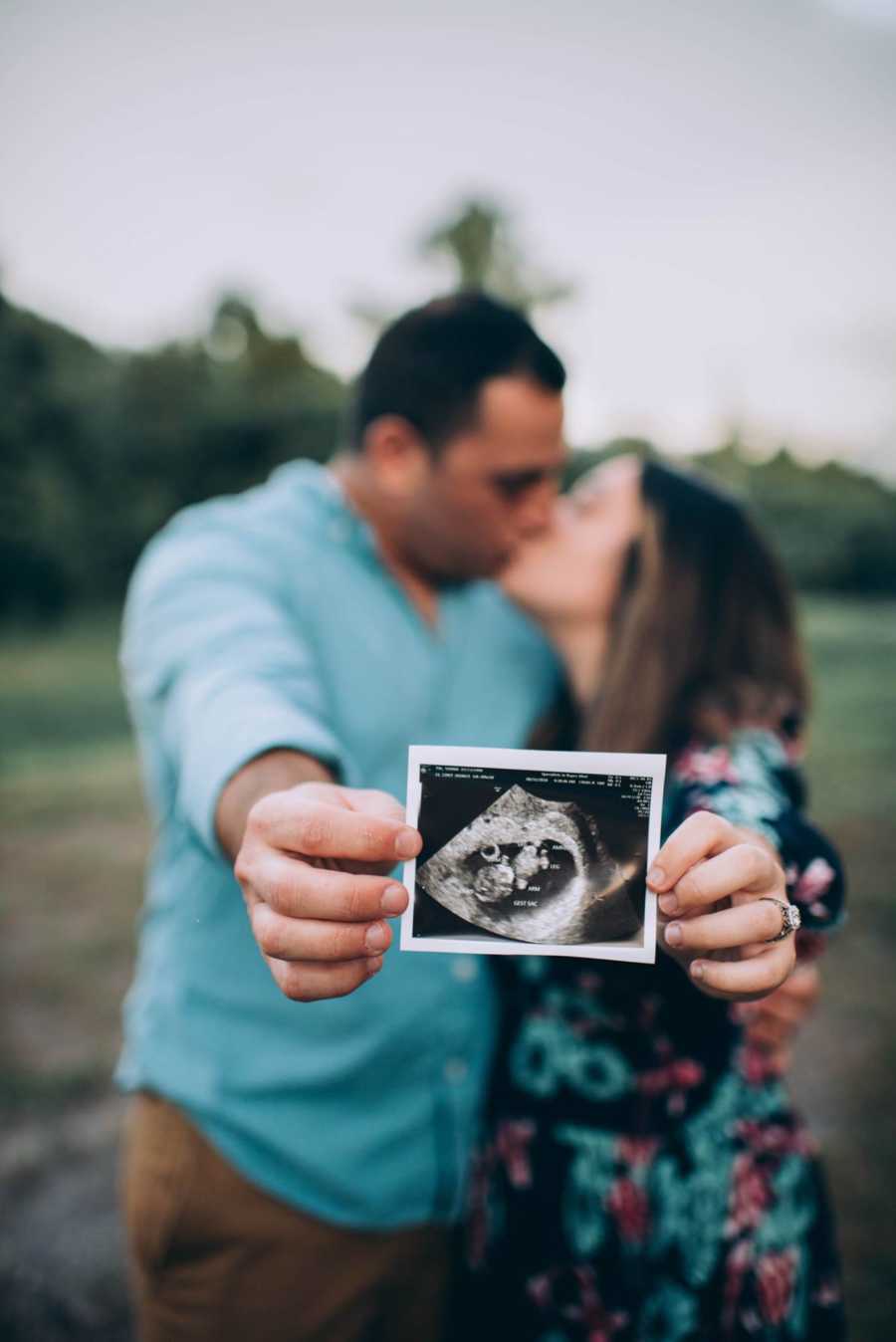 Close up of sonogram husband and wife are holding while they kiss in background