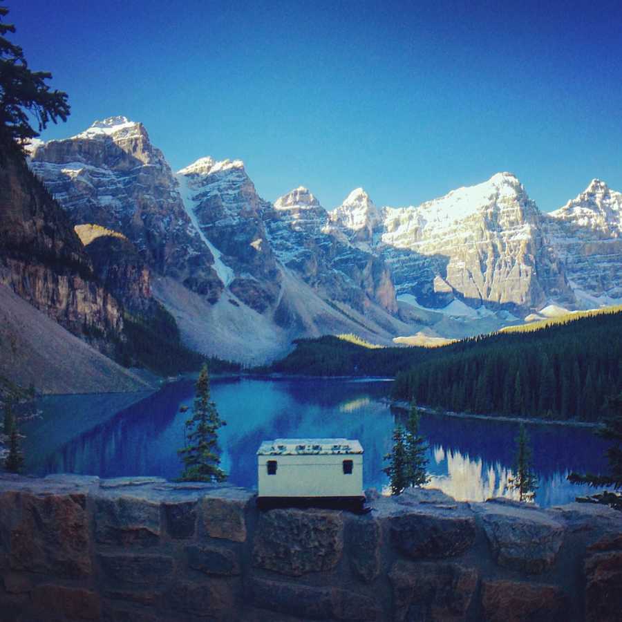 Box of woman's ashes sitting on stone wall with body of water and snowy mountains in background