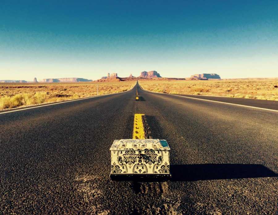 Box of woman's ashes sitting in middle of road in desert with canyons in background