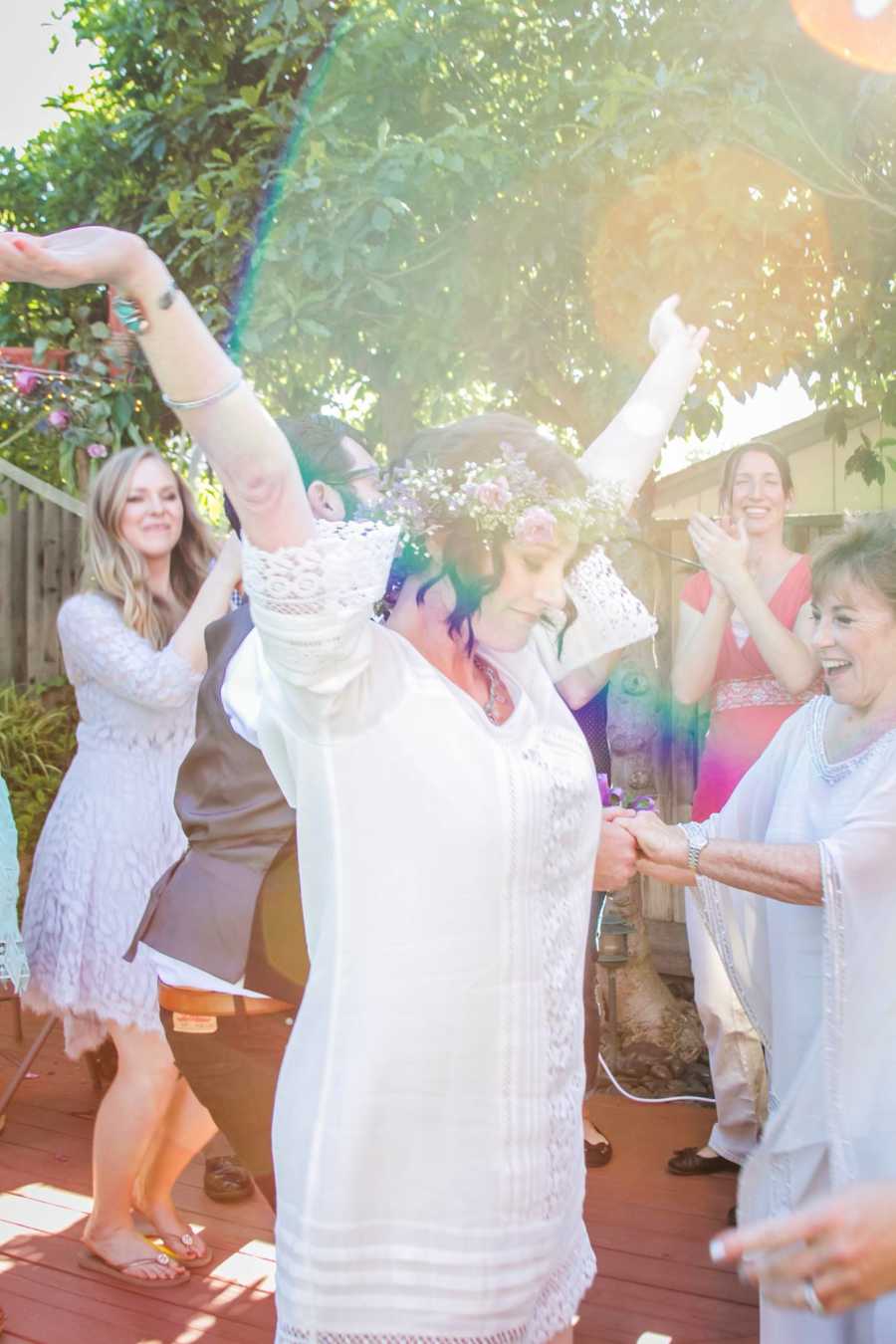 Bride with cancer stands with hands in air as people look at her smiling
