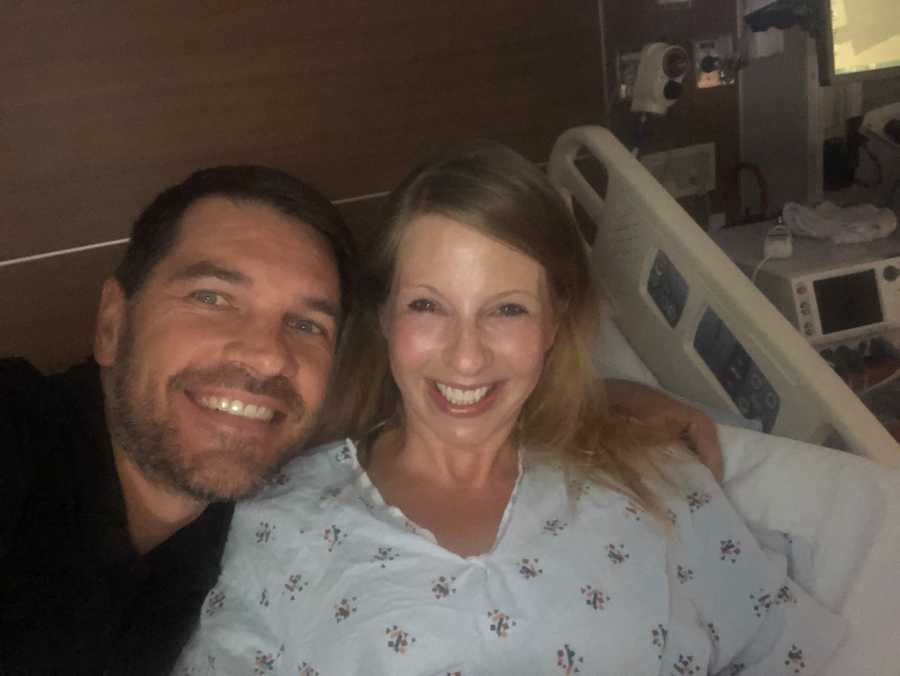 Woman pregnant via IVF smiles in hospital bed beside husband in selfie