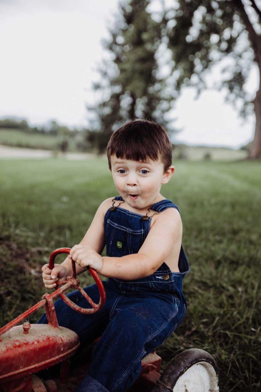 Little boy makes funny face while sitting on toy red tractor