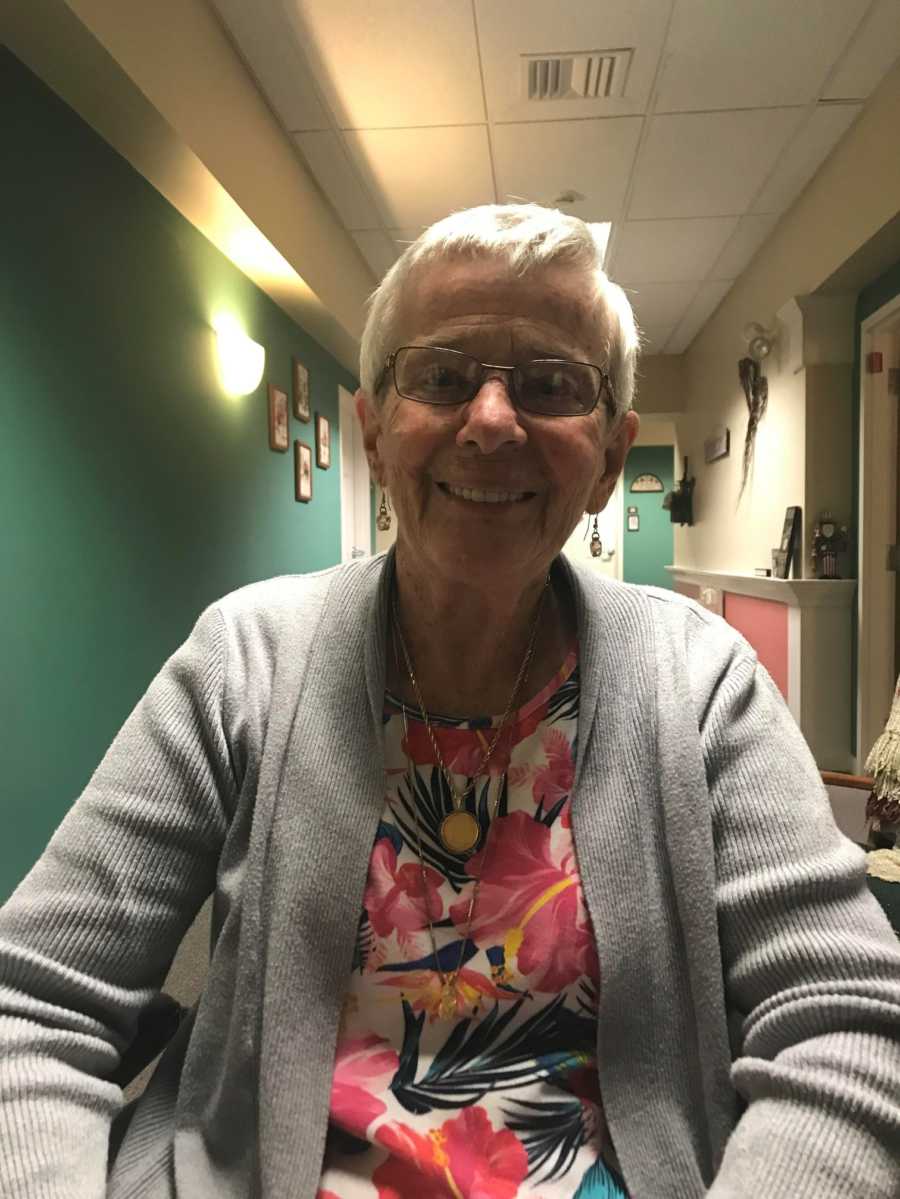 Elderly woman with dementia smiles in gray sweater and floral top