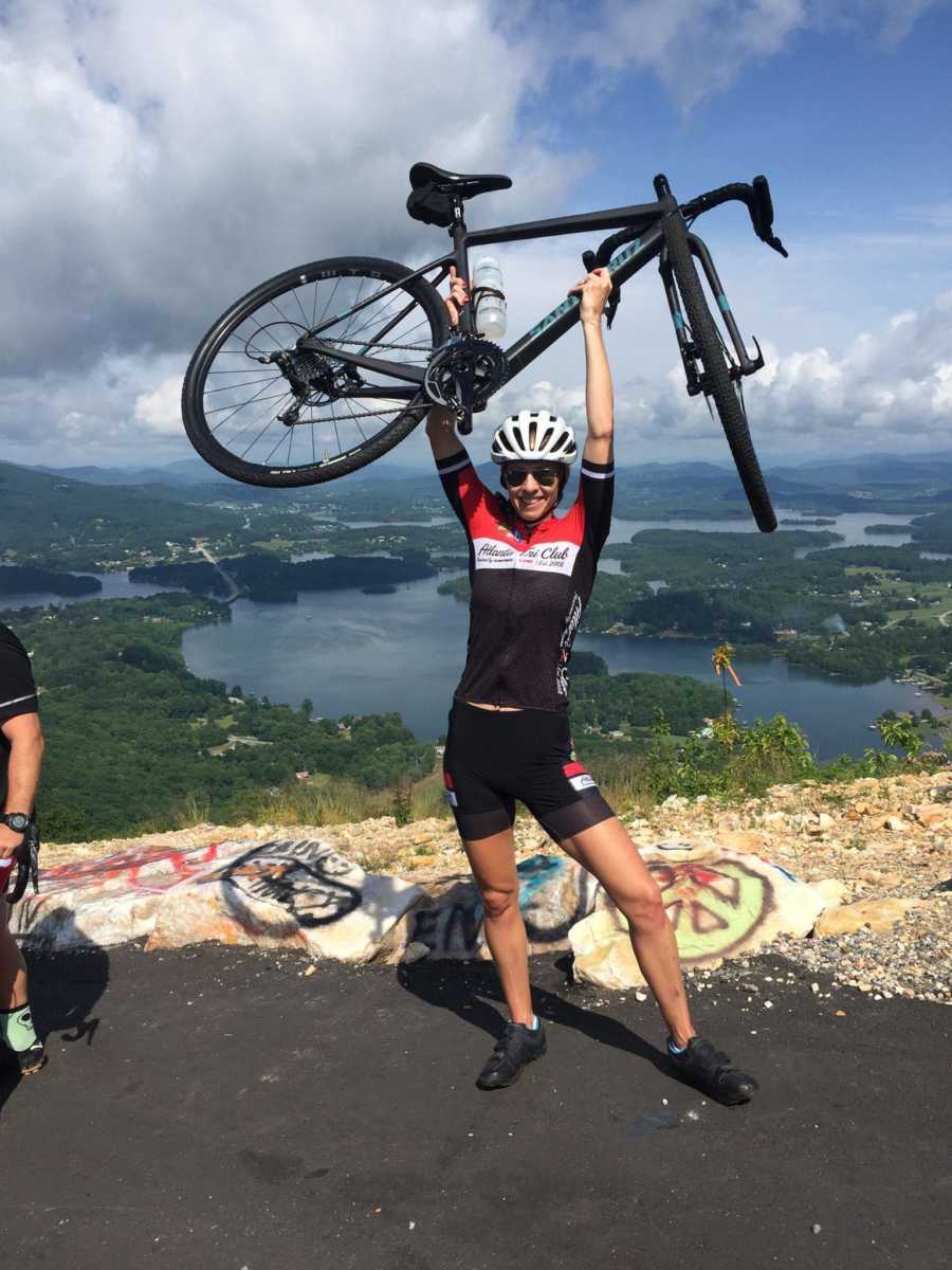 Woman who struggles with fertility holds bike above her head after completing an Iron Man Race