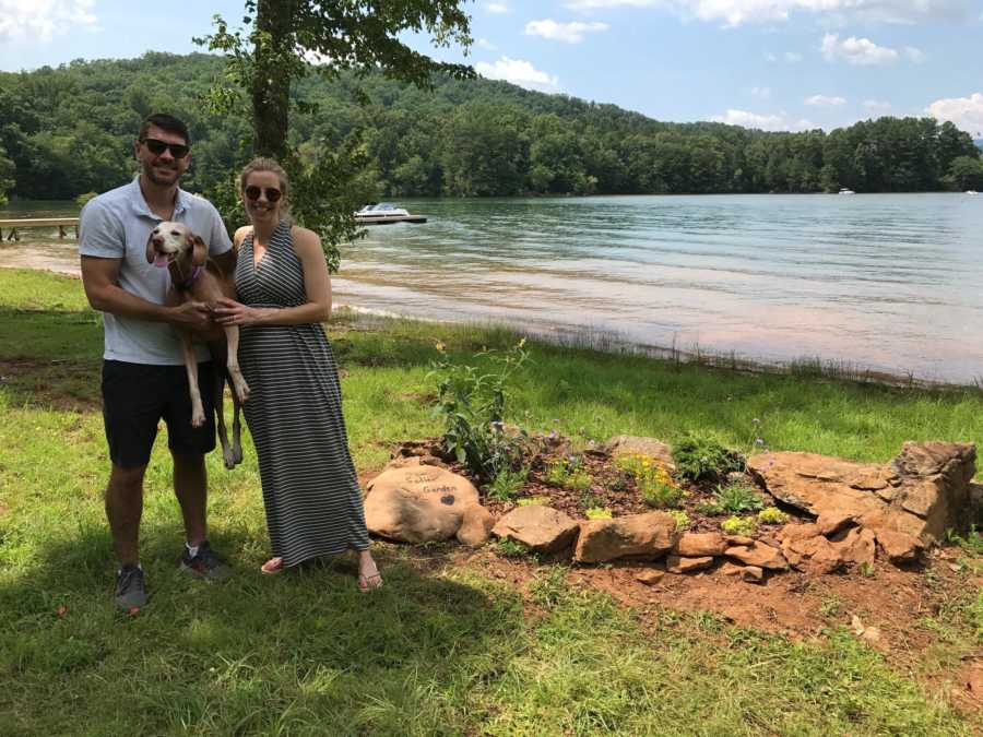 Woman who was pregnant via IVF stands next to husband as they hold dog near body of water
