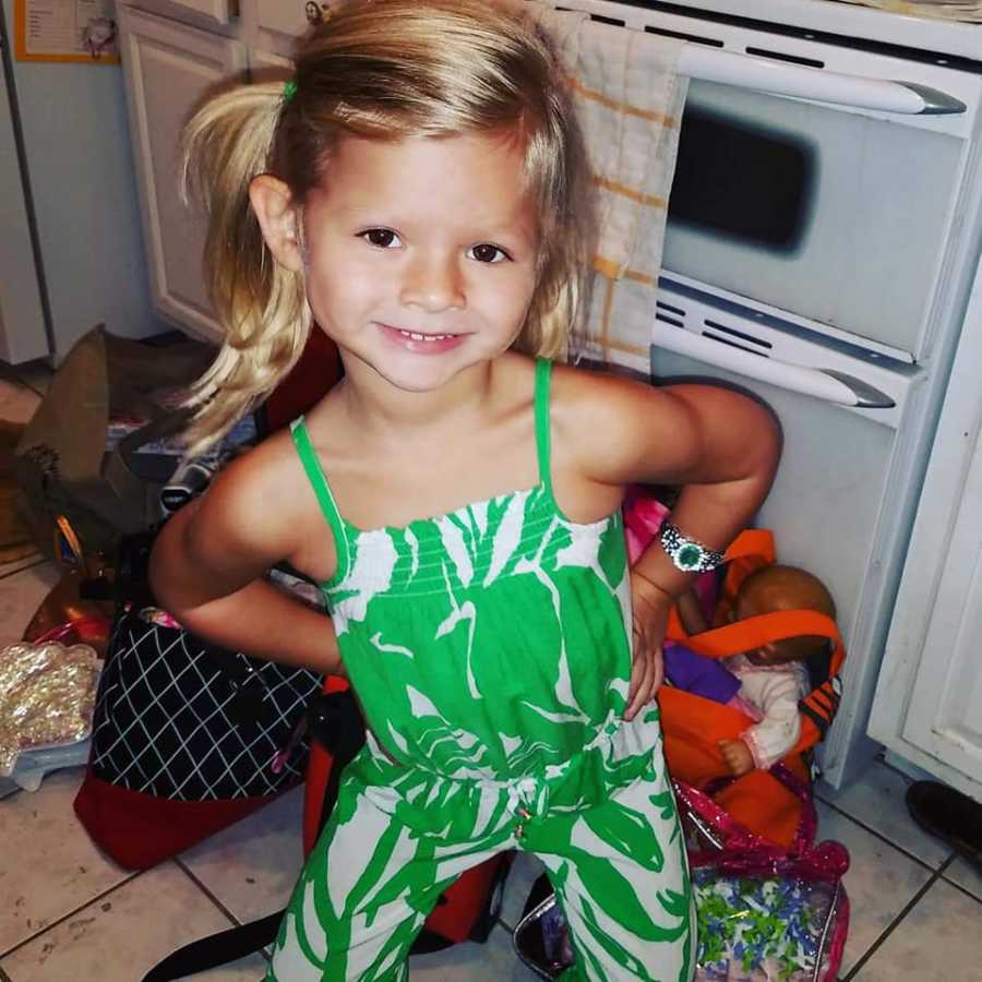 Little girl who has passed away from sepsis stands smiling with hands on her hips in kitchen