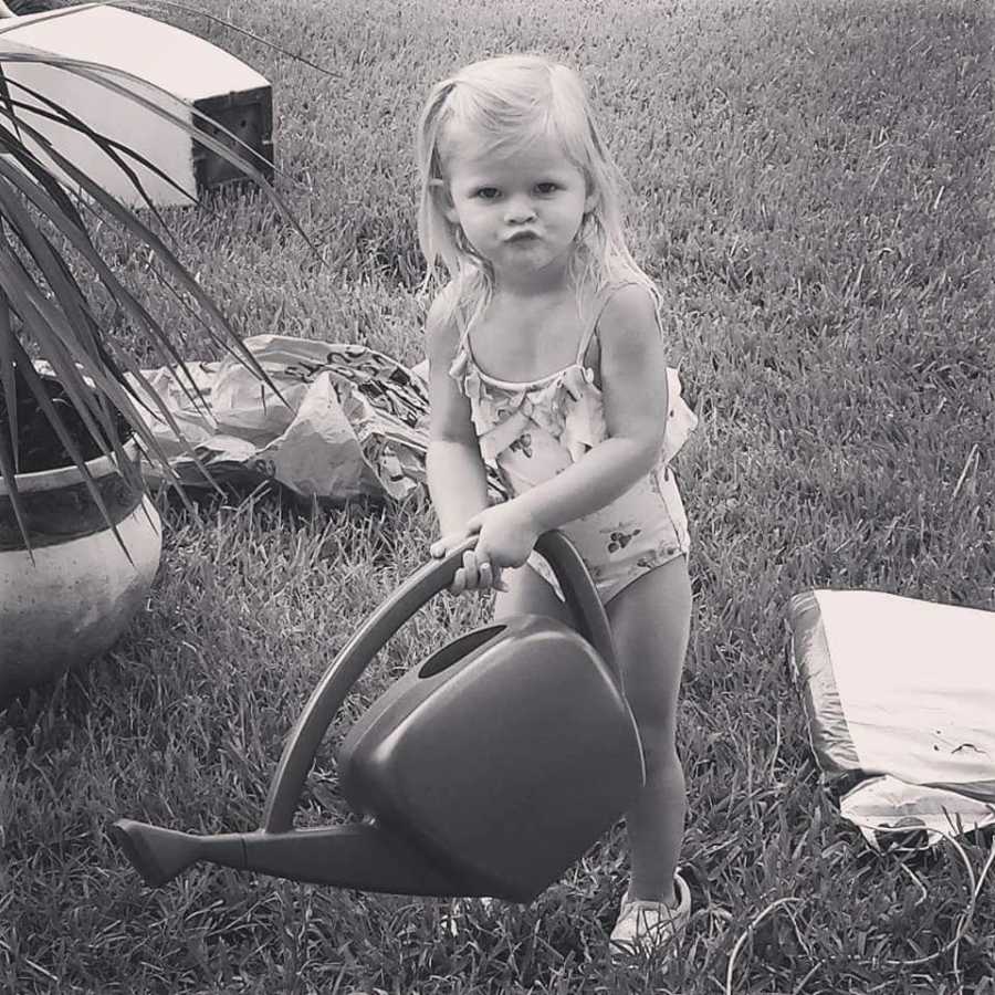 Toddler with sepsis wearing bathing suit in yard while holding watering can