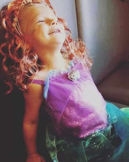 Little girl with sepsis smiling while sitting on couch wearing a princess Ariel costume