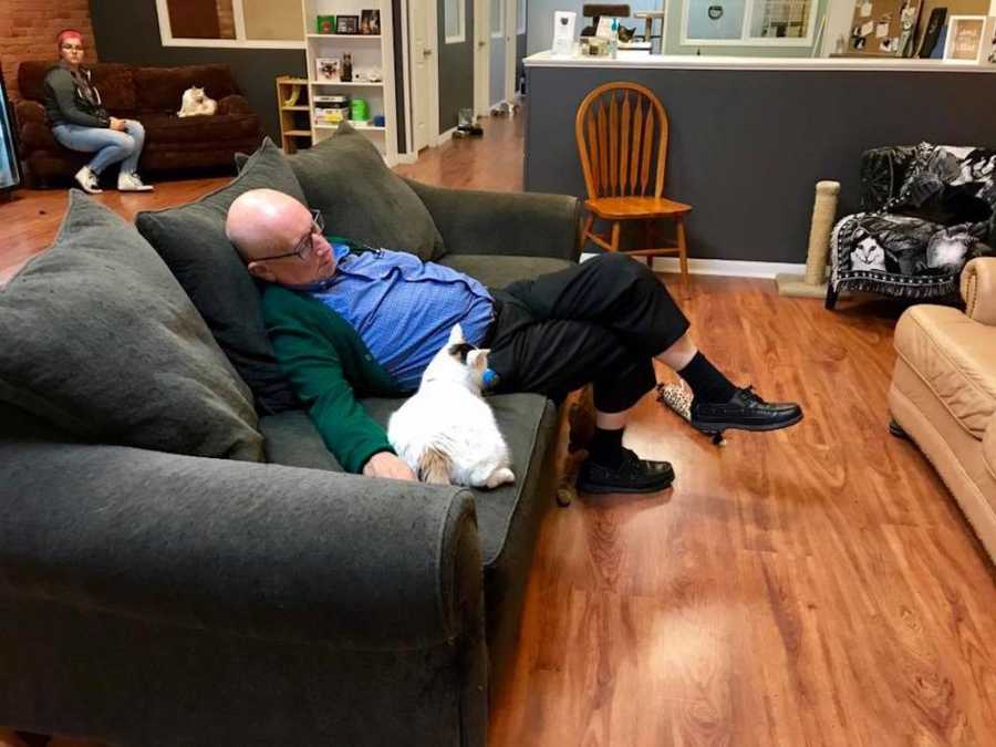 Man asleep on couch of cat shelter with cat laying beside him