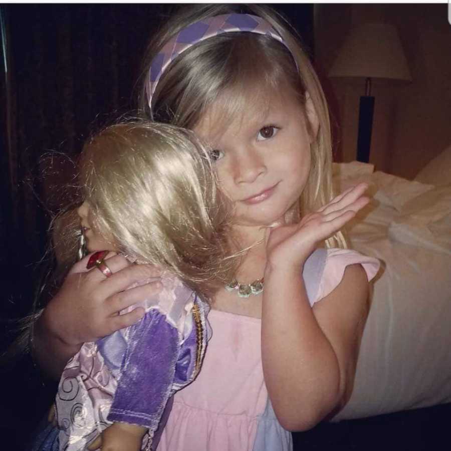 Little girl with sepsis posing with hand on her chin while holding American Girl Doll