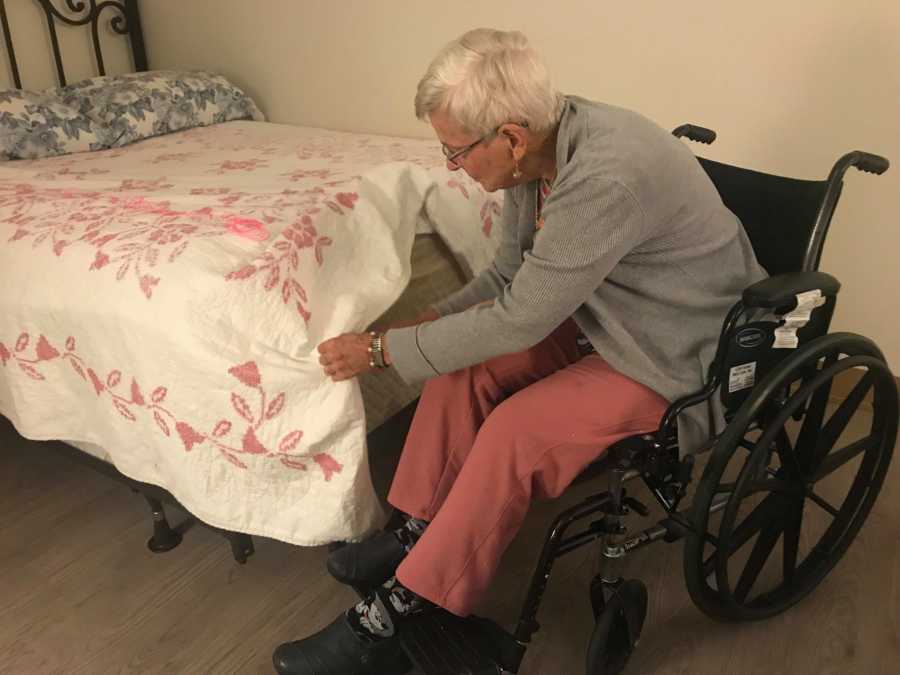 Elderly woman with dementia sits in wheelchair making her bed in nursing home
